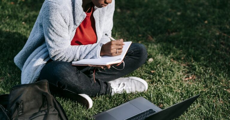 Estudante de pesquisa trabalhando em laptop e caderno em mesa limpa com foco sério.