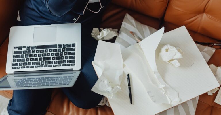 Pesquisador escrevendo relatório acadêmico em laptop com notas temáticas ao lado em ambiente profissional