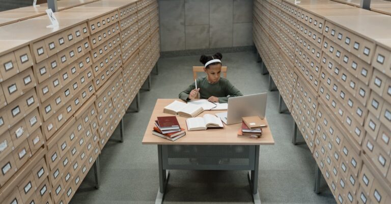 Estudante doutoranda organizando referências em laptop e caderno em ambiente de estudo limpo
