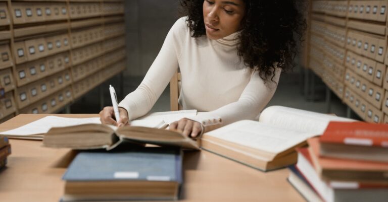 Mulher pesquisadora lendo artigos acadêmicos em mesa clara com laptop e notas organizadas.