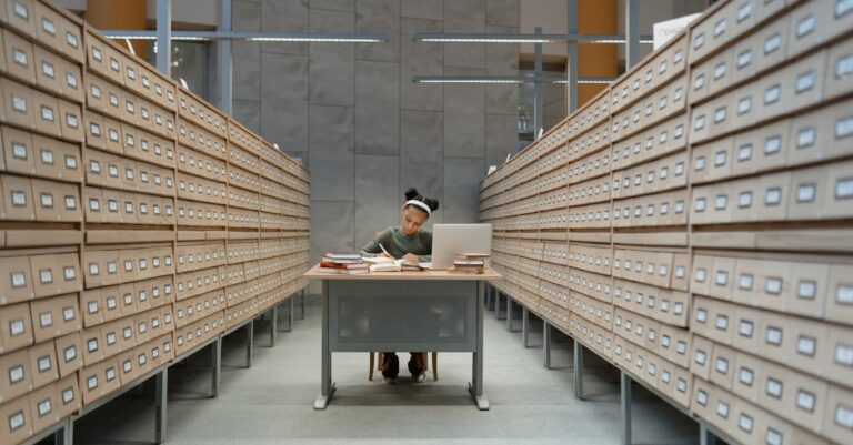 Pesquisador listando premissas críticas em caderno ao lado de tela de computador