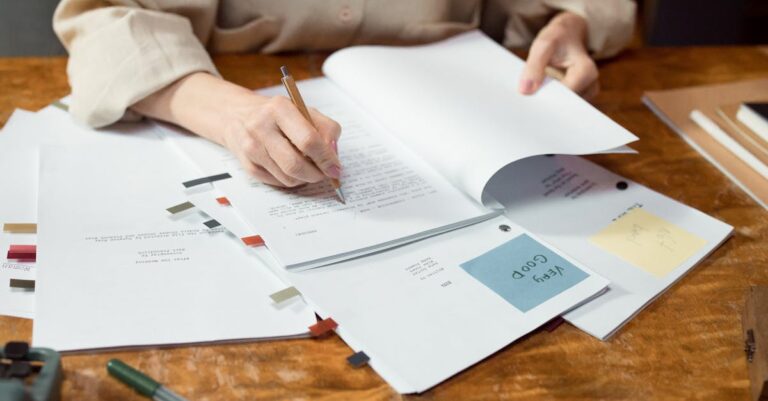 Pesquisador analisando roteiro de entrevista em papel com laptop ao fundo em escritório minimalista