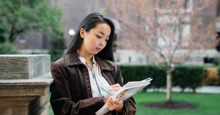 Pesquisadora revisando literatura em caderno anotado com laptop ao lado em ambiente minimalista