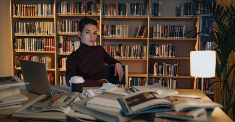 Pesquisadora confiante trabalhando em laptop com documentos acadêmicos ao fundo claro