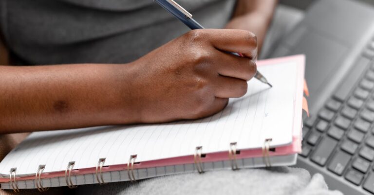 Pesquisador escrevendo relatório final de análise temática em laptop em setup clean