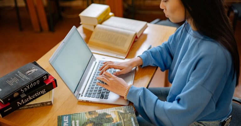 Estudante pesquisador trabalhando concentrado em laptop com notas estatísticas.