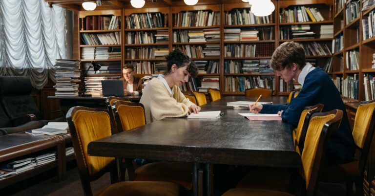 Estudante pesquisador escrevendo notas em caderno com laptop aberto em mesa minimalista